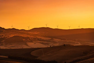 A serene landscape showing wind turbines on rolling hills at sunset.