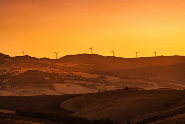 A serene landscape showing wind turbines on rolling hills at sunset.