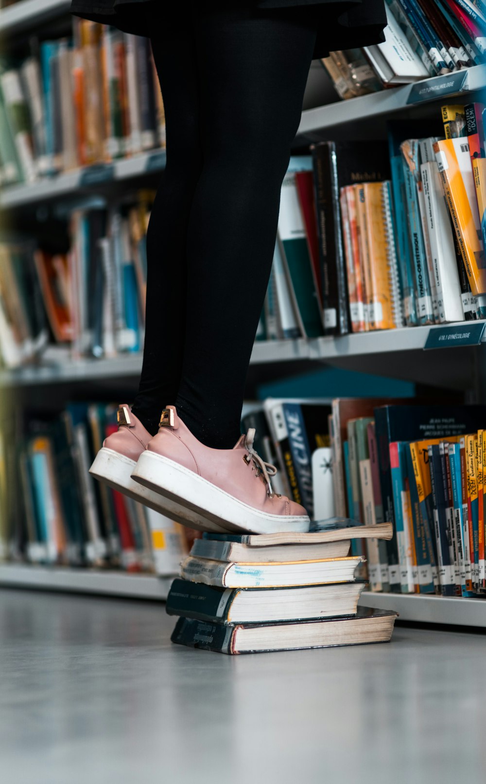 person using books for boosting beside bookcase with books