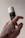 A hand with a tattooed design holds a cylindrical container with a black label and white cap. The label reads 'KORRES', 'Pinho Negro', and 'Black Pine'. The background is a neutral, soft color, highlighting the product and the hand.