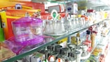 A display shelf is filled with various kitchen items including salt and pepper shakers, spice containers, and condiment jars. Brightly colored plastic and glass containers are arranged neatly. There are also packaged goods like salt and pepper sets in boxes.