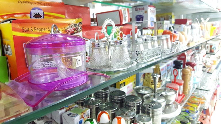 A display shelf is filled with various kitchen items including salt and pepper shakers, spice containers, and condiment jars. Brightly colored plastic and glass containers are arranged neatly. There are also packaged goods like salt and pepper sets in boxes.
