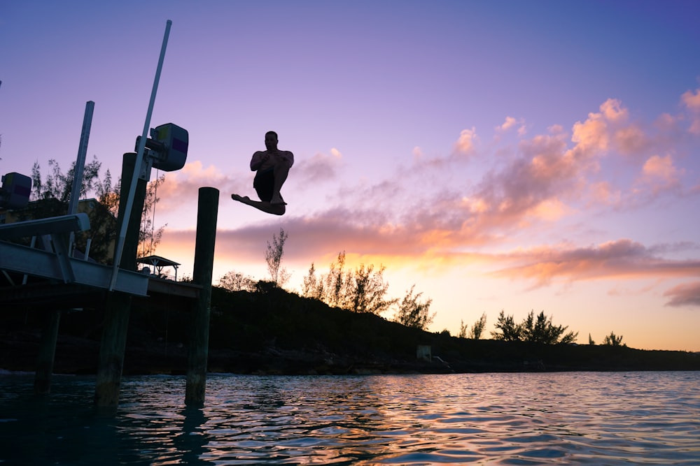 topless man jumping on lake under orange and blue skies