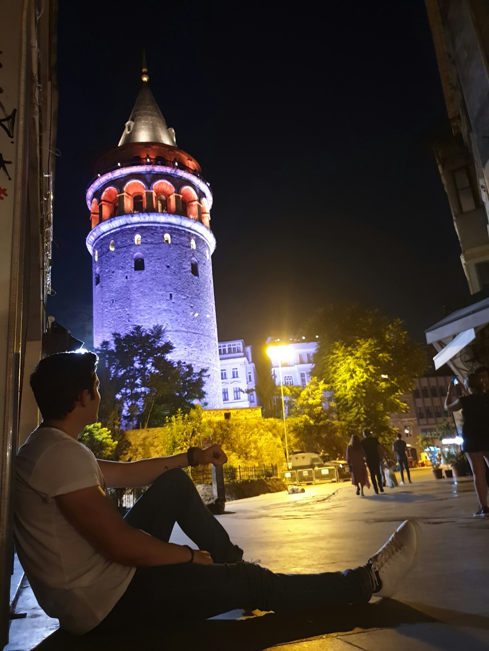 man wearing white shirt and black pants sitting on concrete floor during night time