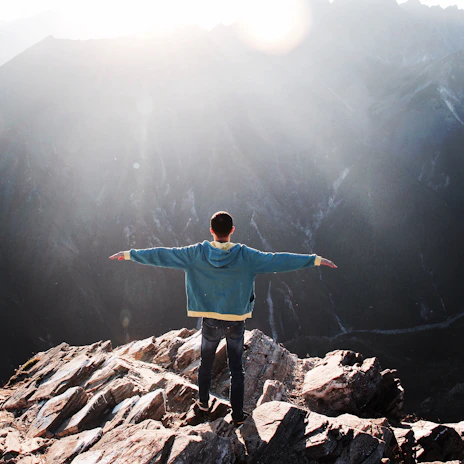 An adventurous traveler standing on a cliff edge, arms wide open, with a vast mountain range ahead.