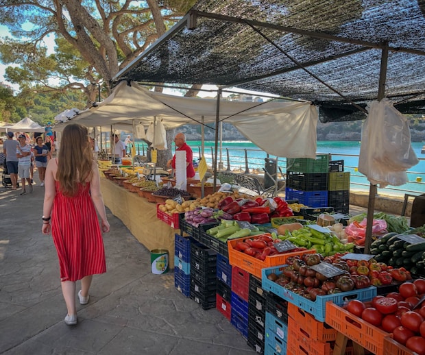 woman walking beside fruit and vegetable vendors at a market in Mallorca
