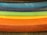 A series of fabric rolls in various bright colors are stacked horizontally. Each roll displays a distinct hue, creating a gradient effect from dark to light shades.