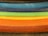 A series of fabric rolls in various bright colors are stacked horizontally. Each roll displays a distinct hue, creating a gradient effect from dark to light shades.