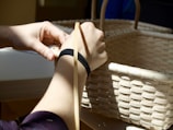 Close-up of hands weaving bamboo strips into a basket in a sunny outdoor setting.