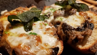 Two pieces of toasted bread topped with melted cheese, mushrooms, and fresh herbs. The cheese is bubbly and golden brown, and the herbs add a pop of green color.
