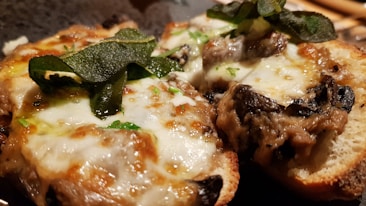 Two pieces of toasted bread topped with melted cheese, mushrooms, and fresh herbs. The cheese is bubbly and golden brown, and the herbs add a pop of green color.