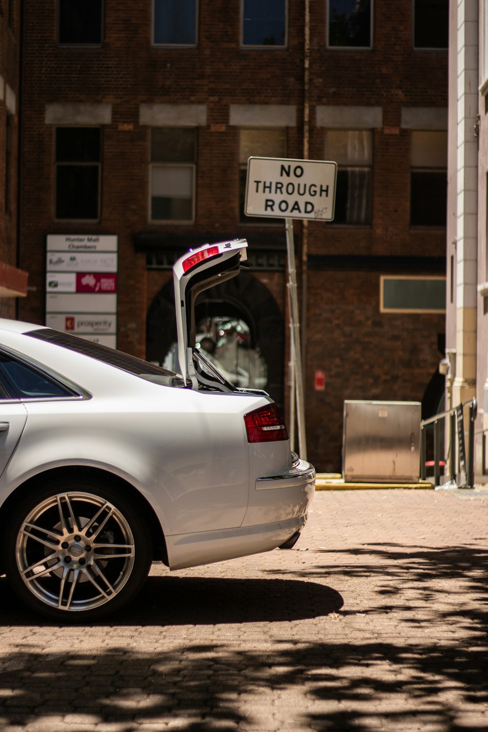 gray car with open trunk parked beside No Through Road sign