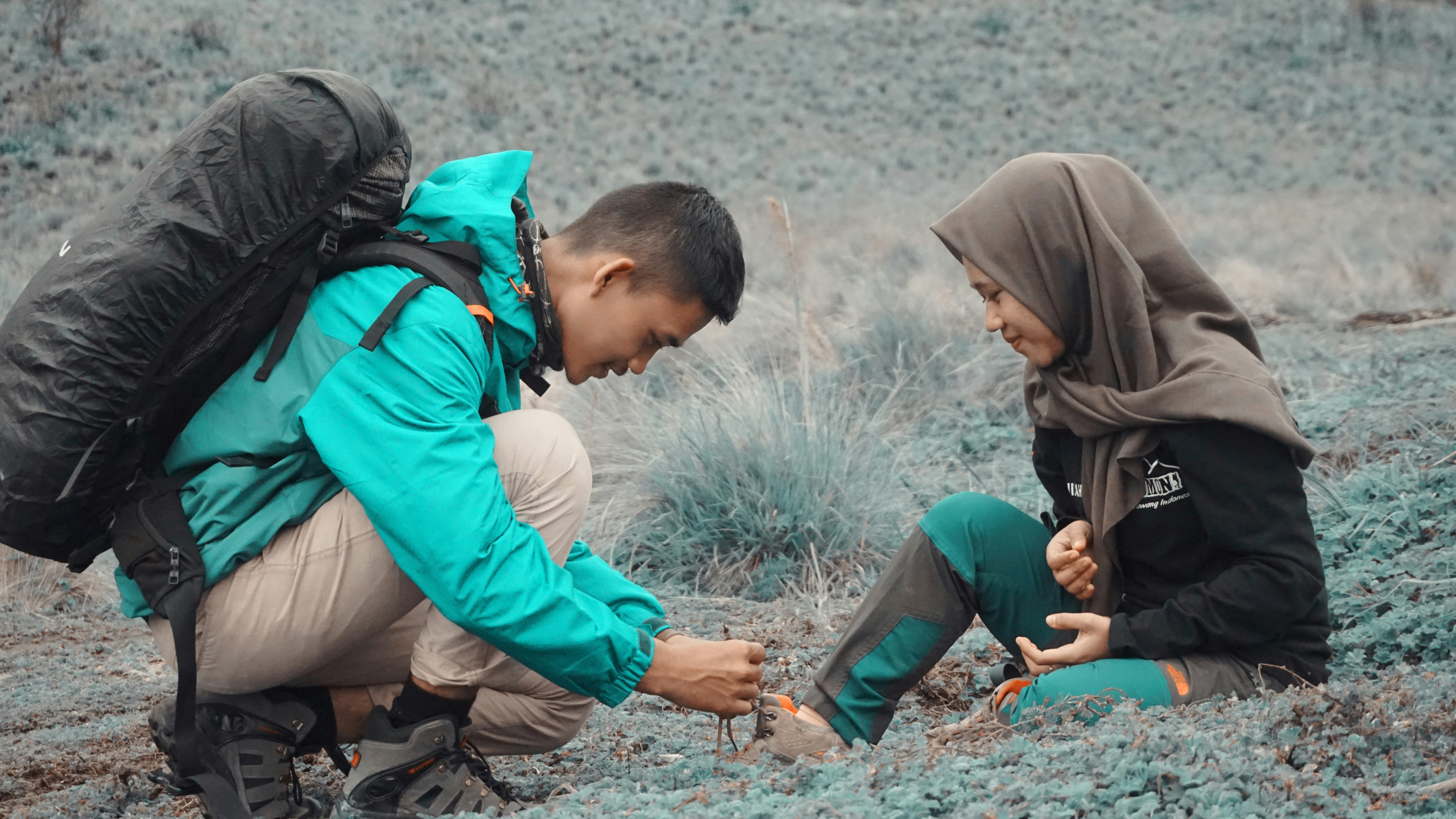 Pria mengenakan jaket teal dan celana krem membawa ransel