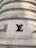 A large stone building wall featuring a prominent black metal logo with the letters 'LV' prominently mounted on its surface. The wall has a series of horizontal, rounded grooves that create a textured appearance. The structure displays an architectural style that suggests strength and luxury.