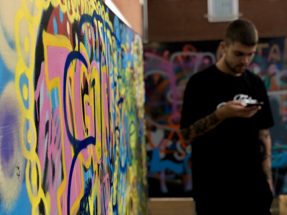 man standing and using smartphone near wall with murals