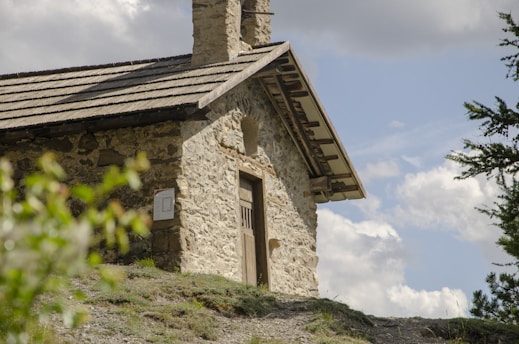A charming stone cottage nestled among rolling green hills of the Peak District under a bright blue sky.