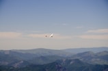 An intermediate pilot soaring above lush green mountains under a clear blue sky.