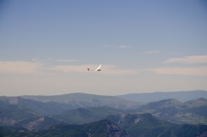 An intermediate pilot soaring above lush green mountains under a clear blue sky.