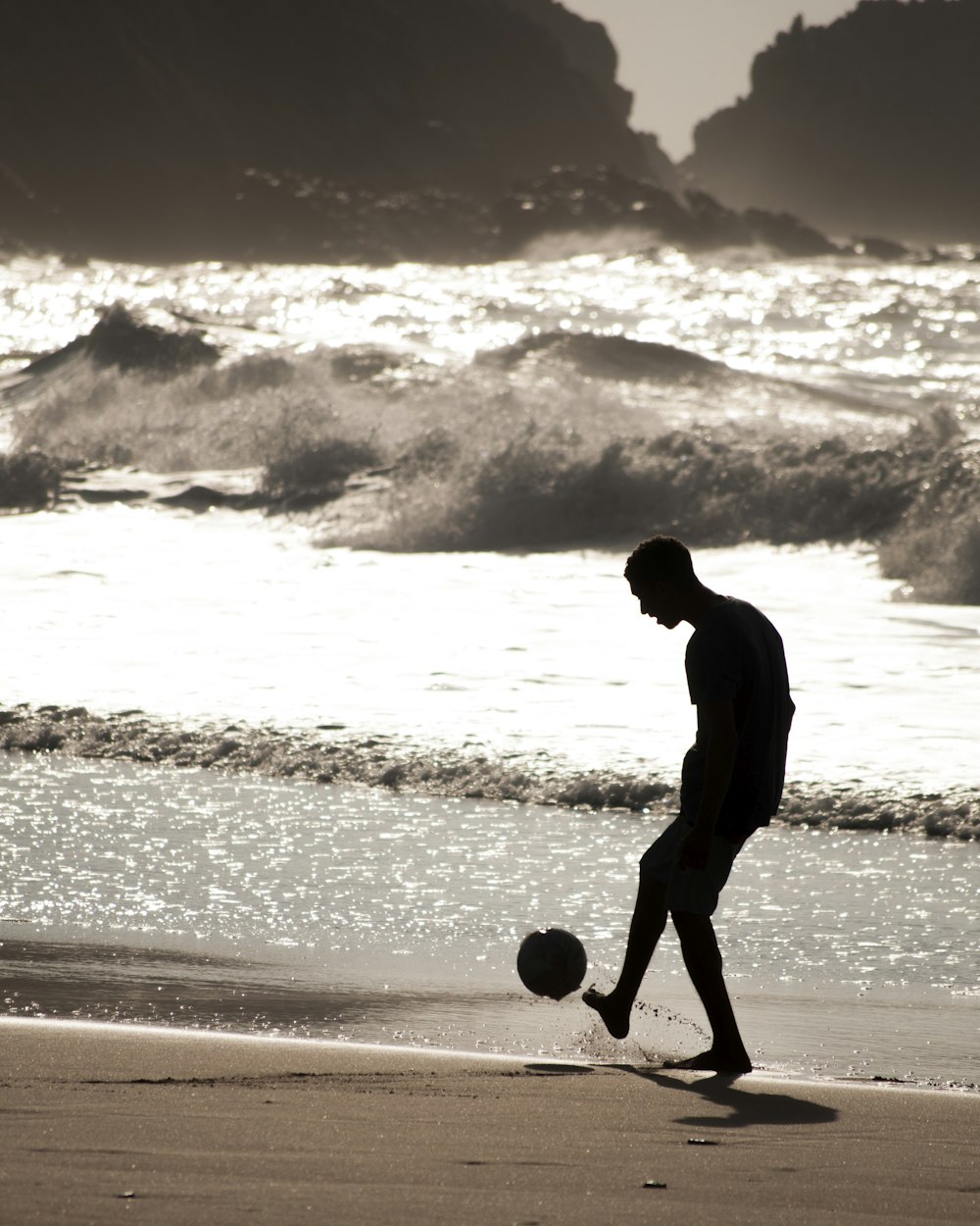 Hombre descalzo jugando con pelota cerca de la orilla del mar