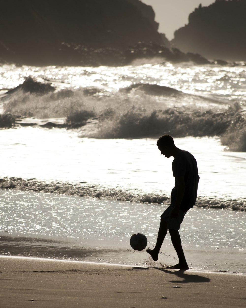 uomo a piedi nudi che gioca con la palla vicino alla riva del mare