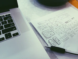 Close-up of hands coding on a laptop keyboard with design sketches beside.