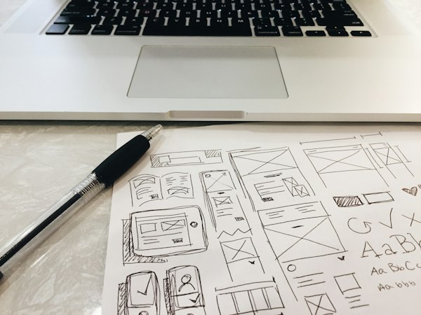 Bocetos de estructura de páginas web dibujados a lápiz sobre papel junto a una laptop, el punto de partida de una agencia de diseño web B2B