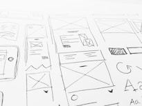 A detailed sketch of web design layouts, featuring boxes, arrows, and various shapes representing components of a webpage. The designs include placeholders for images and text, with lines and symbols indicating structure.