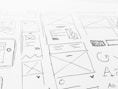 A detailed sketch of web design layouts, featuring boxes, arrows, and various shapes representing components of a webpage. The designs include placeholders for images and text, with lines and symbols indicating structure.