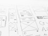 A detailed sketch of web design layouts, featuring boxes, arrows, and various shapes representing components of a webpage. The designs include placeholders for images and text, with lines and symbols indicating structure.