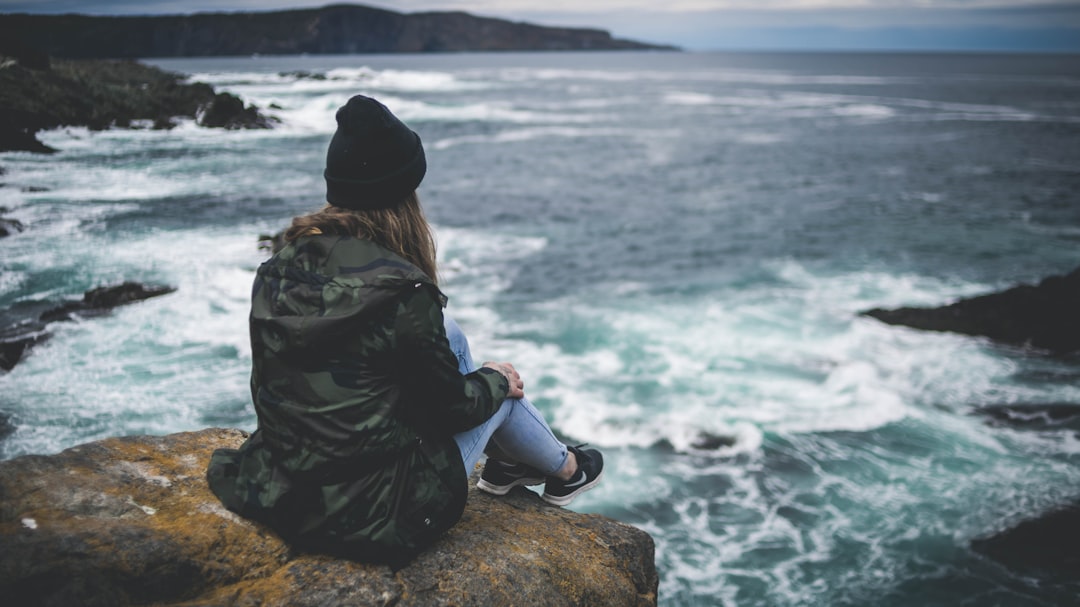 woman sitting on cliff near sea during daytime