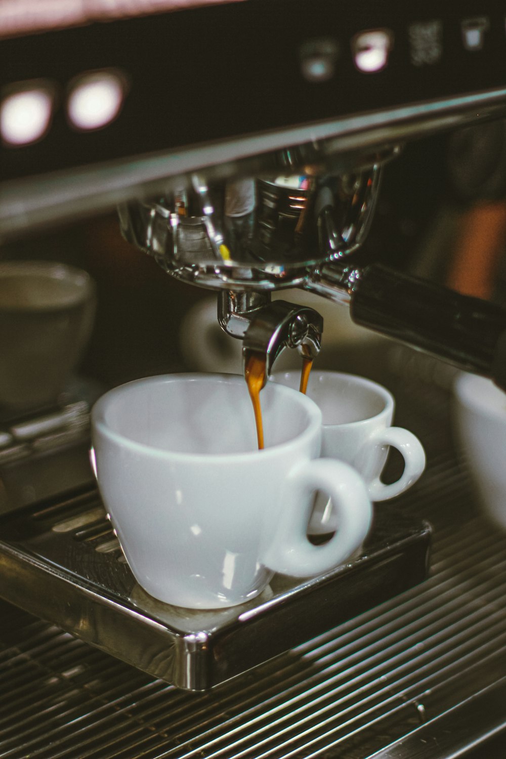 selective focus photography of machine pouring coffee on two mugs