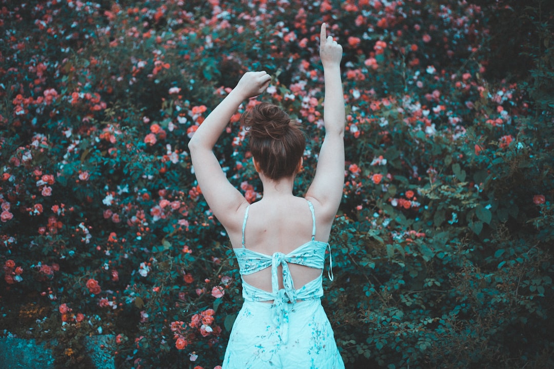 woman standing while raising both hands and facing back on flowers