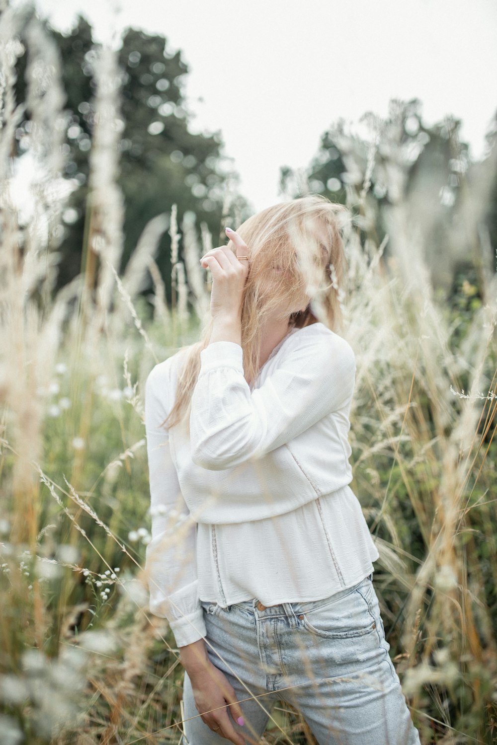 woman in white long sleeved shirt and blue denim jeans standing n middle of grass field