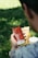 A person is holding a smartphone displaying a subscriber count on the screen, with the number 15,501,615 visible alongside a small profile picture. In the background, a fast-food drink cup and a paper bag sit on the grass, suggesting a casual outdoor environment.