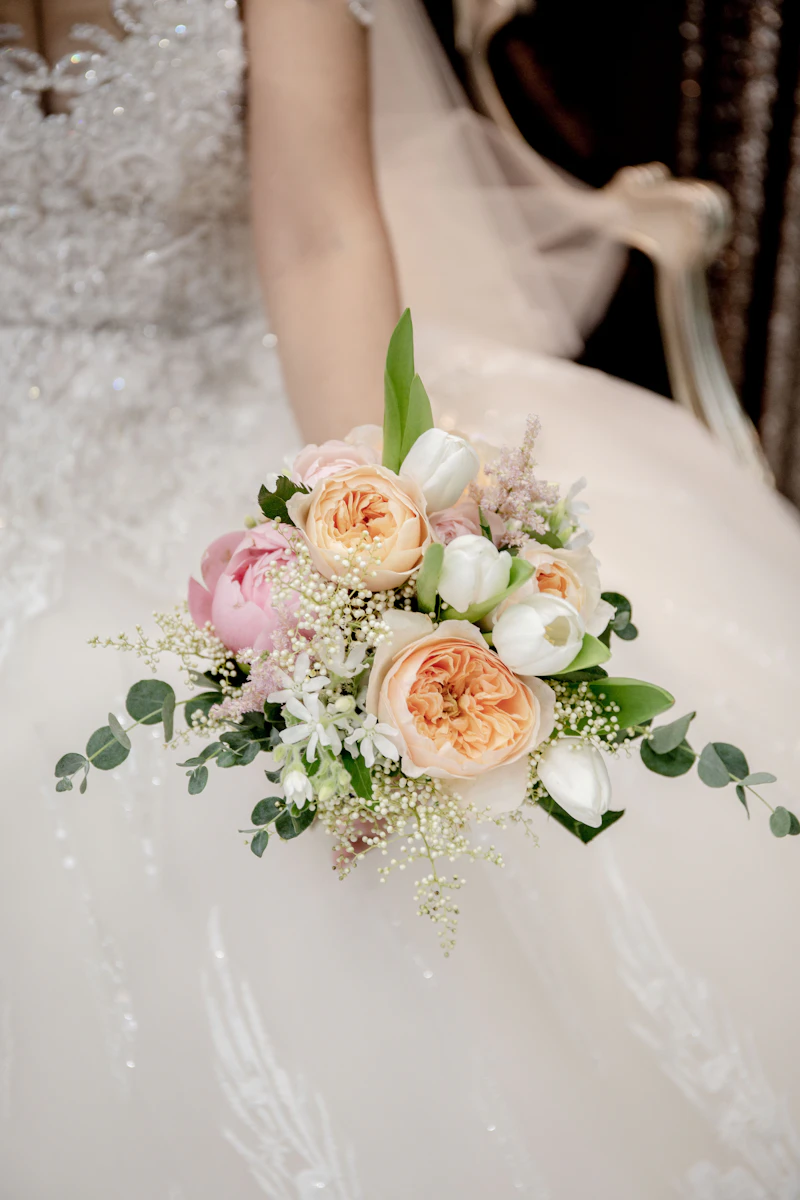 Peach and pink bridal bouquet held against a beaded gown