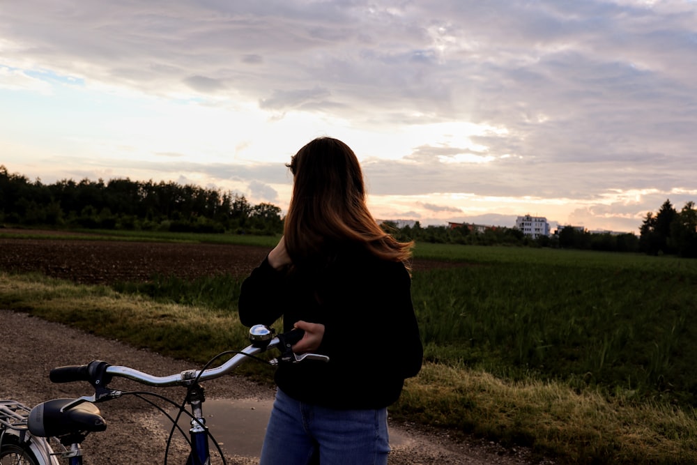 woman standing on dirt road holding bicycle