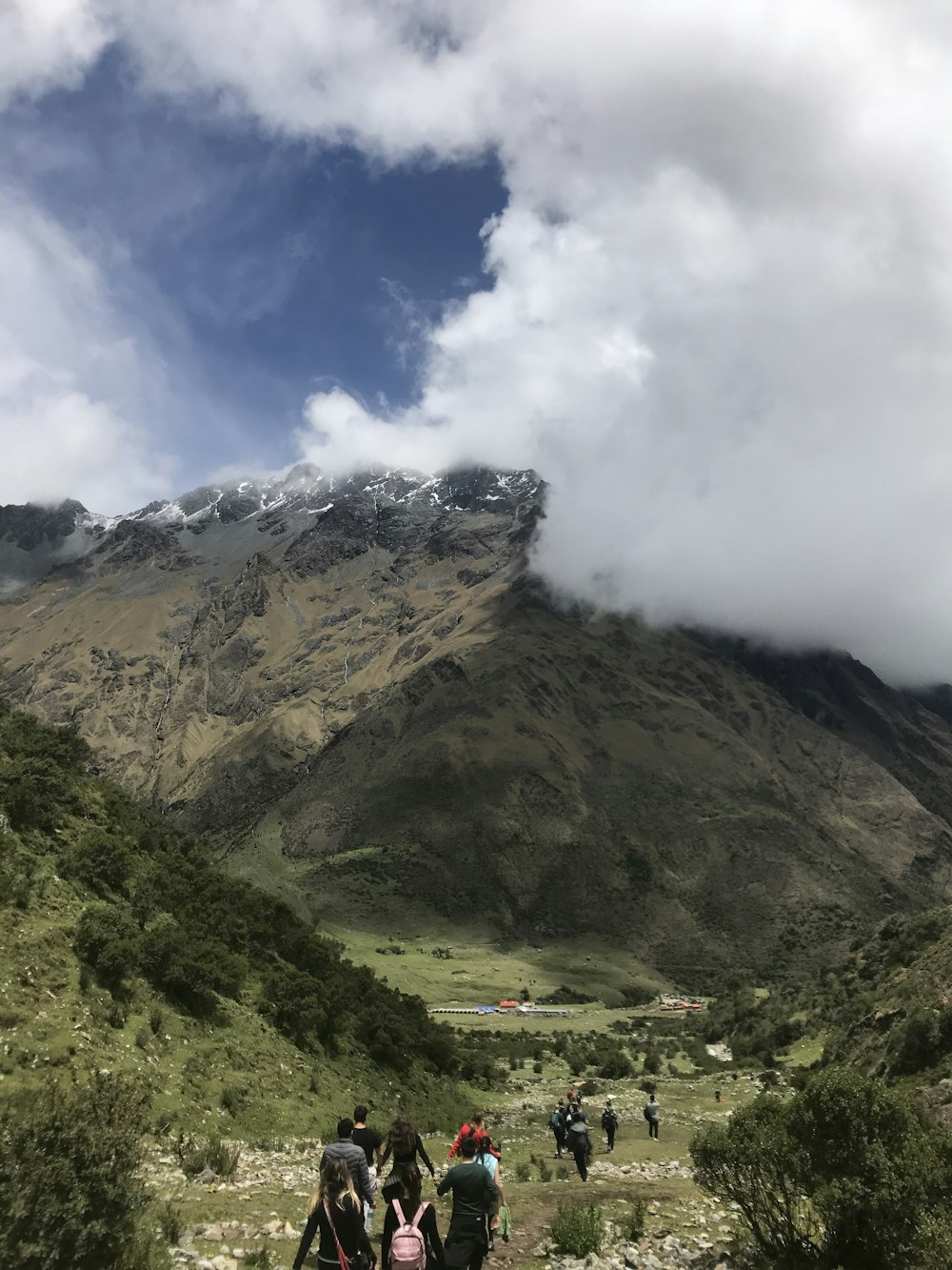 people waking on mountain under white clouds