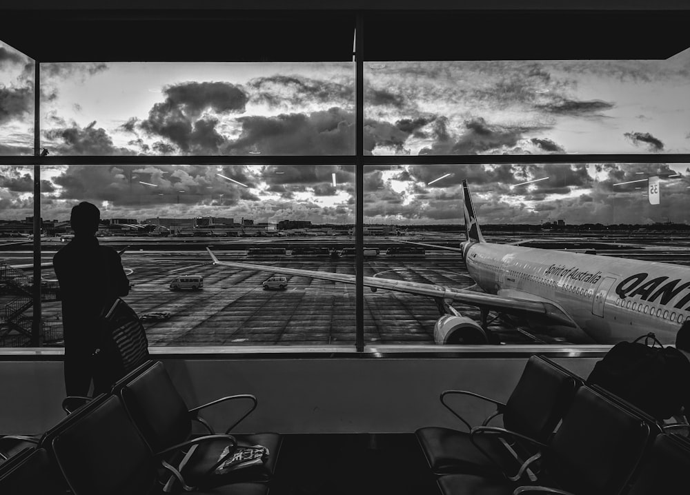 grayscale photography of man standing in front of plane