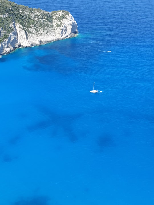 white sailboat in blue sea passing white rock cliff in Shipwreck Beach Greece