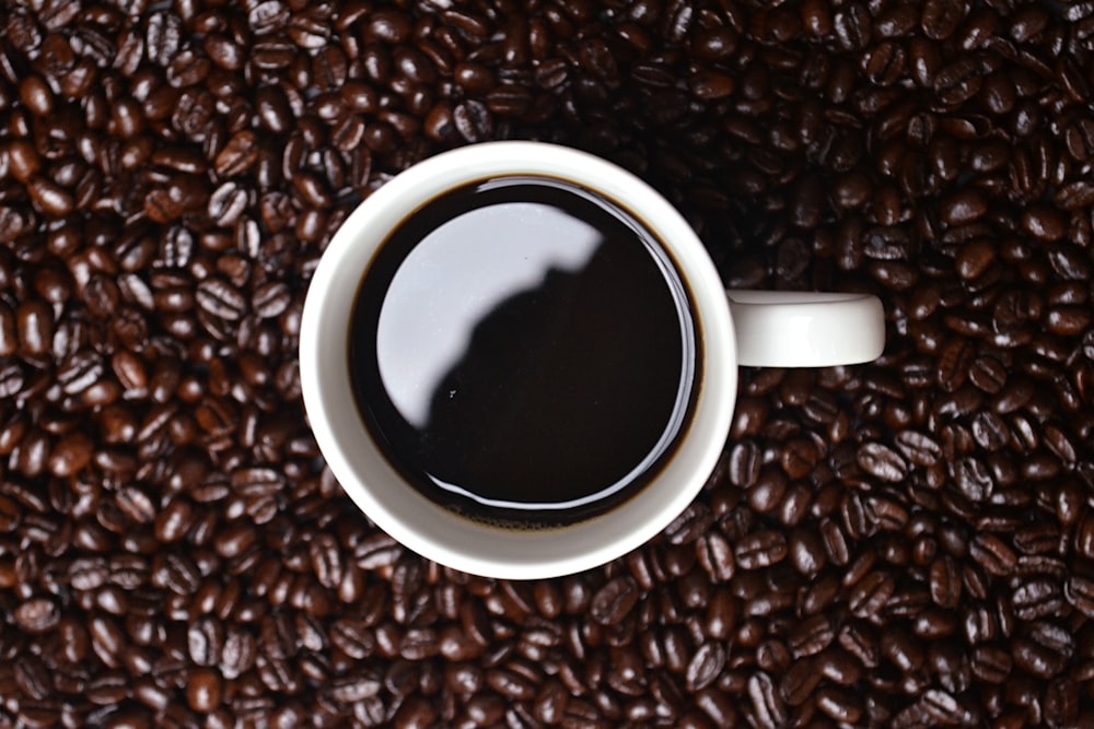 coffee in white ceramic mug on top of brown coffee beans lot