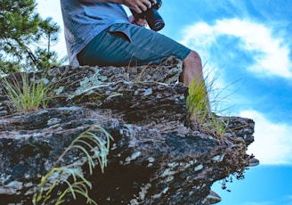 man sitting on creek holding camera