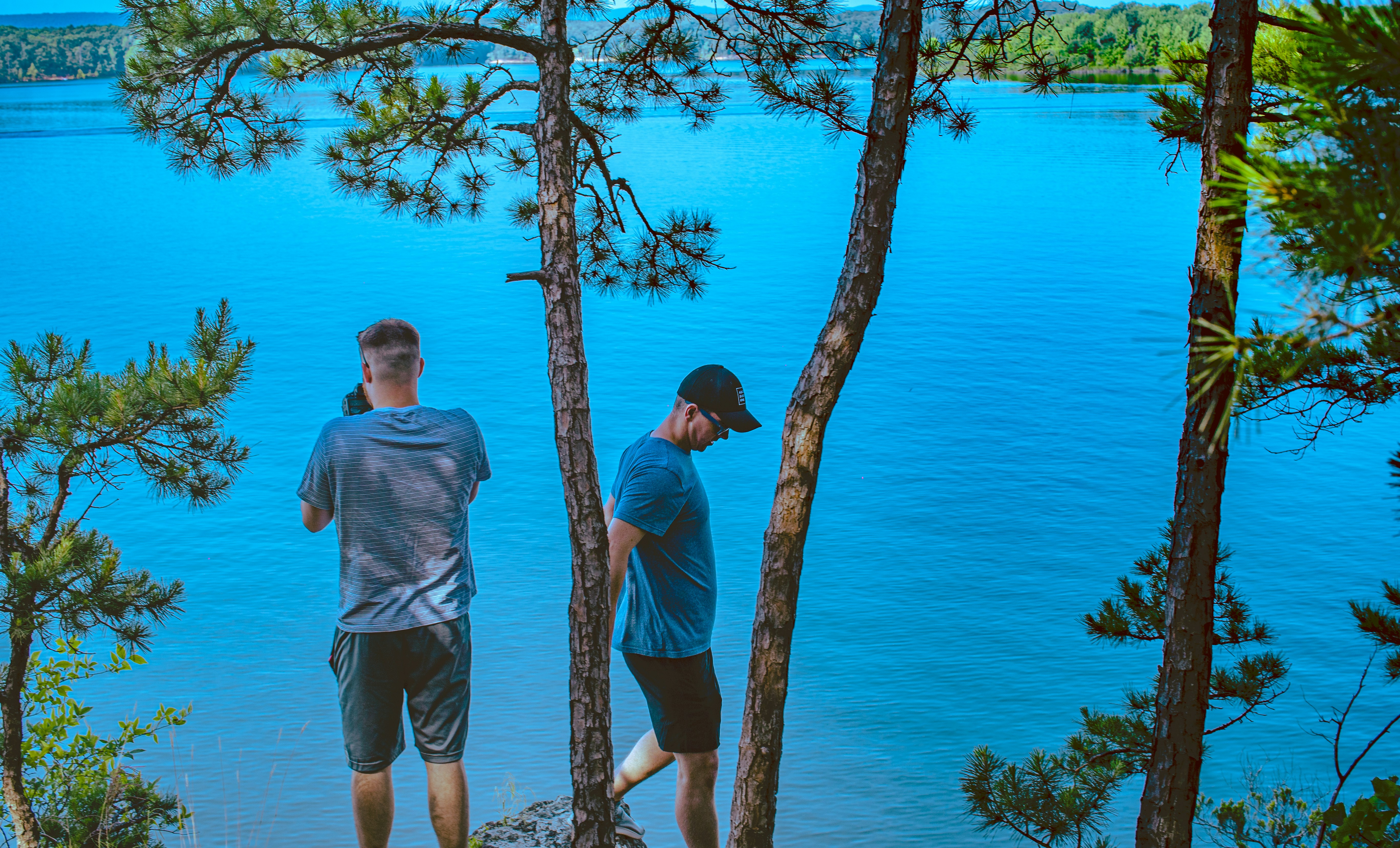 two men standing under trees in bank of lake, 