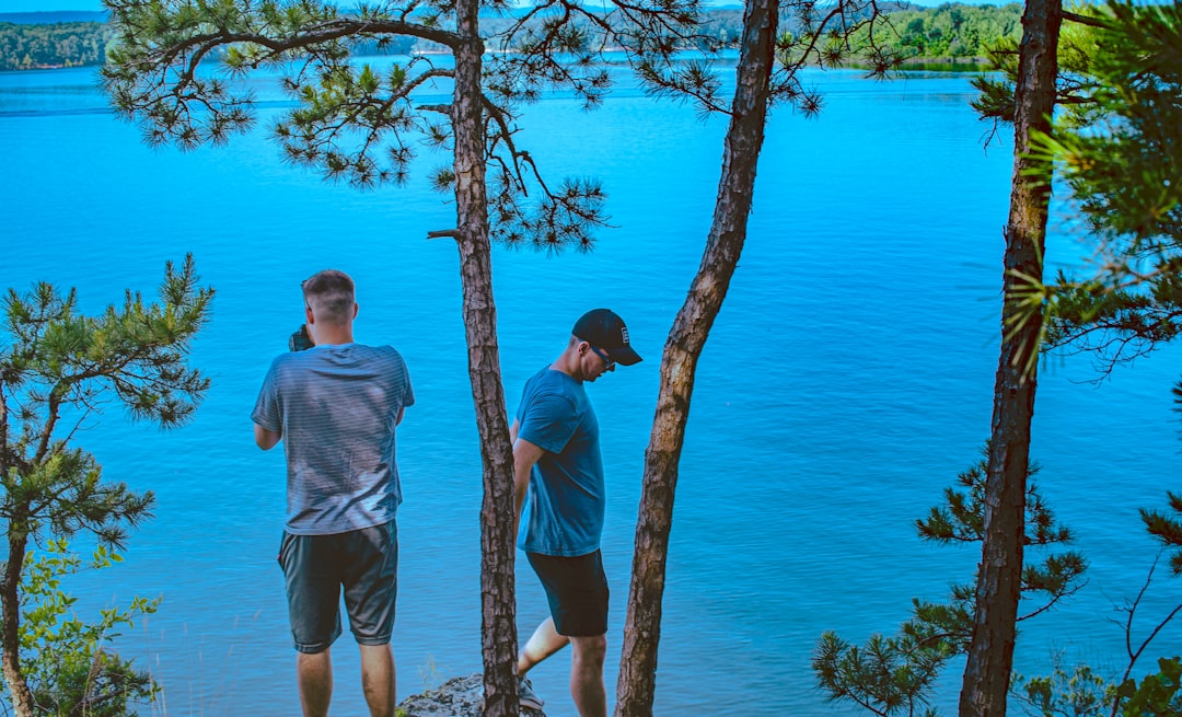 two men standing under trees in bank of lake,