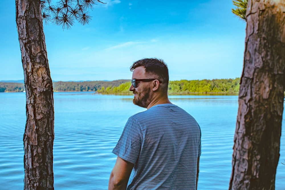 man standing beside tree in front of body of water