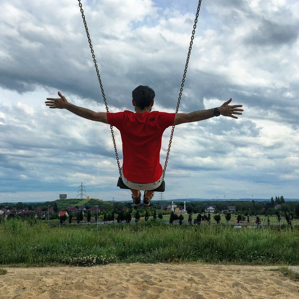 person sitting on outdoor swing raising both hands