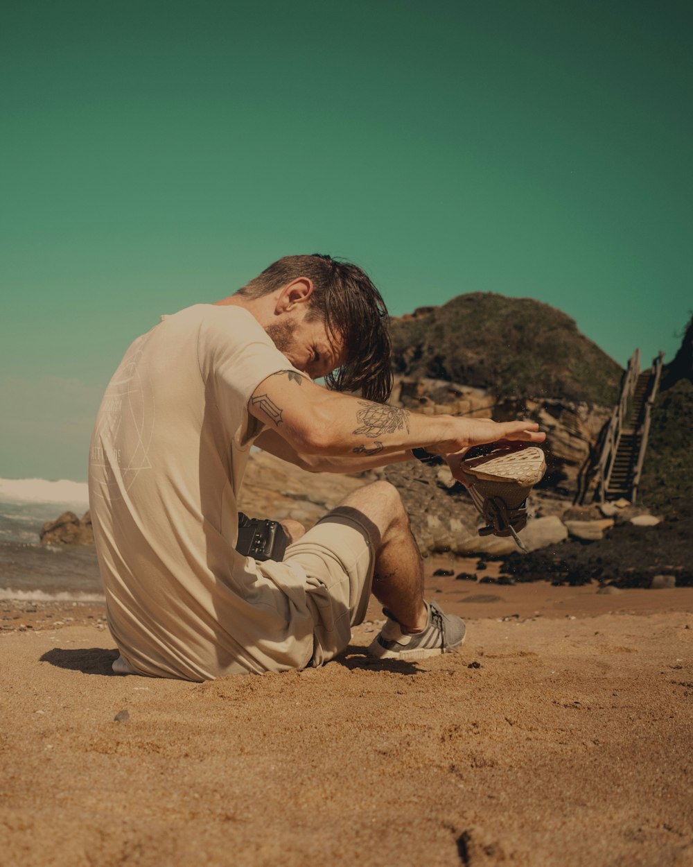 man in white shirt and brown shorts sitting in brown sand beach