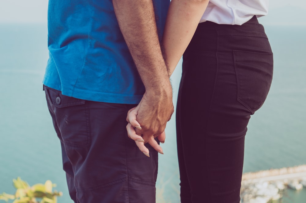 couple holding each other's hand near body of water