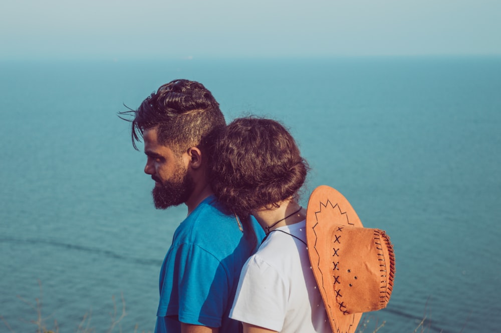 man in blue t-shirt standing in front of woman beside body of water