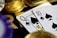 A close-up view of playing cards, specifically a Queen and a Ten of spades, surrounded by shiny gold coins and part of a poker chip, suggesting a gambling or casino theme.