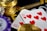 A close-up view of playing cards showing the ten of hearts placed alongside poker chips and a stack of gold coins. The scene suggests a gambling or casino setting with high stakes involved.